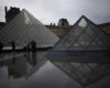 People tour the courtyard of Le Louvre museum in the rain Monday, Oct. 27, 2025 in Paris. (AP Photo/Christophe Ena)