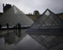 People tour the courtyard of Le Louvre museum in the rain Monday, Oct. 27, 2025 in Paris. (AP Photo/Christophe Ena)