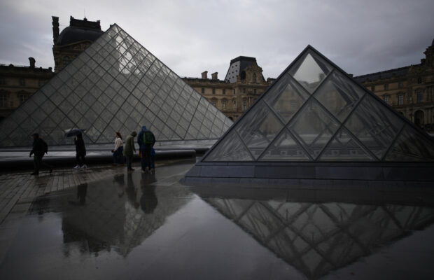 People tour the courtyard of Le Louvre museum in the rain Monday, Oct. 27, 2025 in Paris. (AP Photo/Christophe Ena)