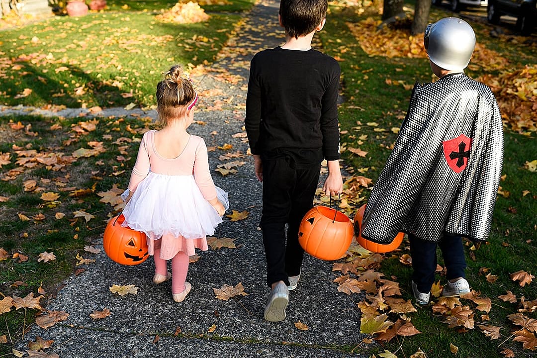 Kids wearing halloween costumes with their trick and treat buckets down the sidewalk.